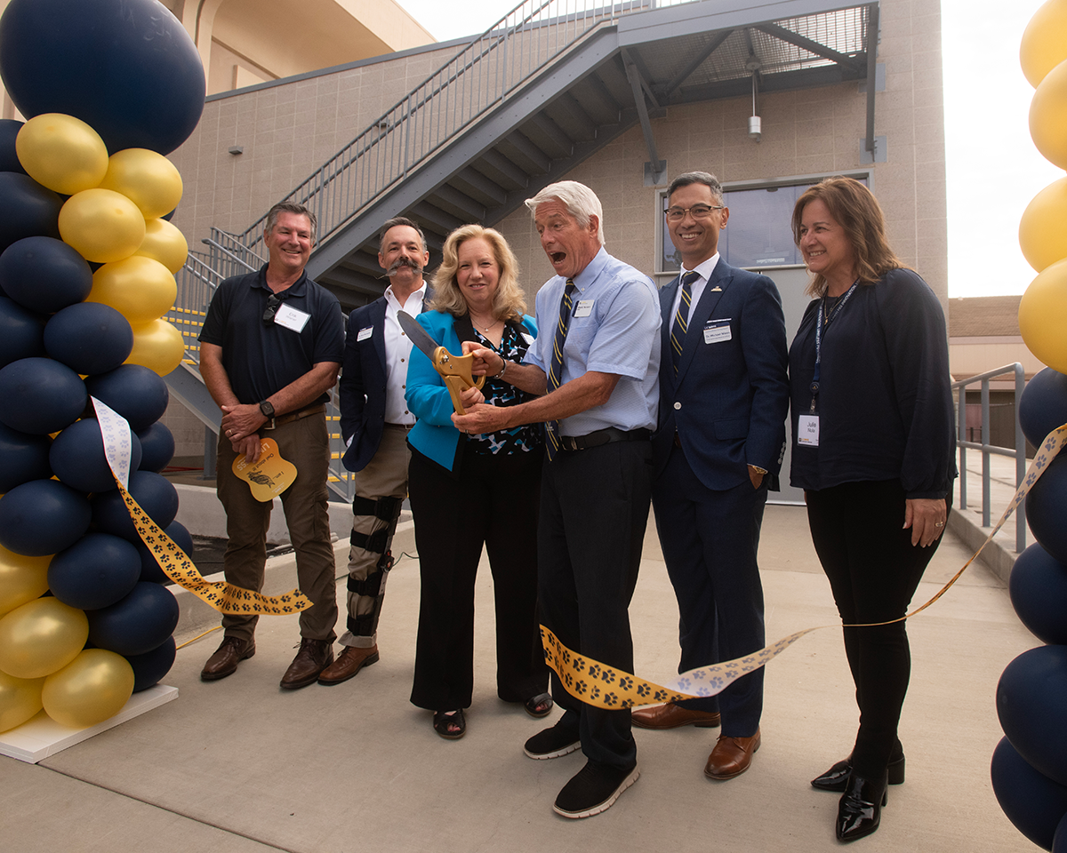 A group standing behind a large ribbon that is being cut with scissors.