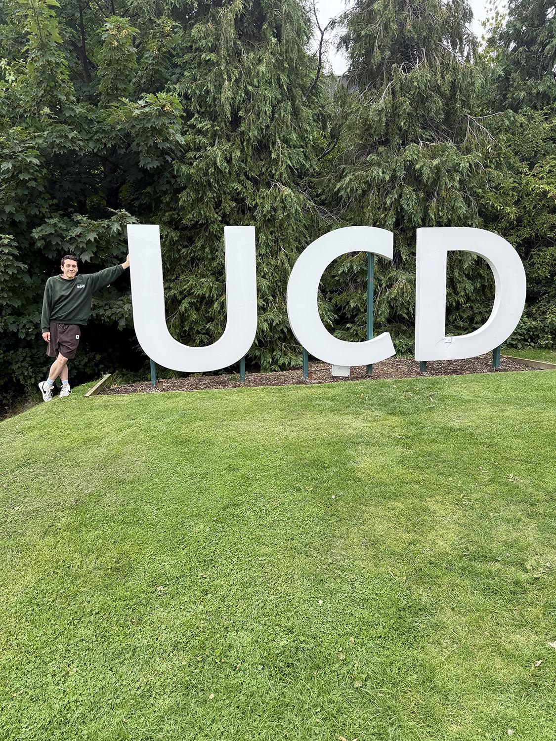 A person leaning on the first letter of a large lawn sculpture of the letters "UCD."