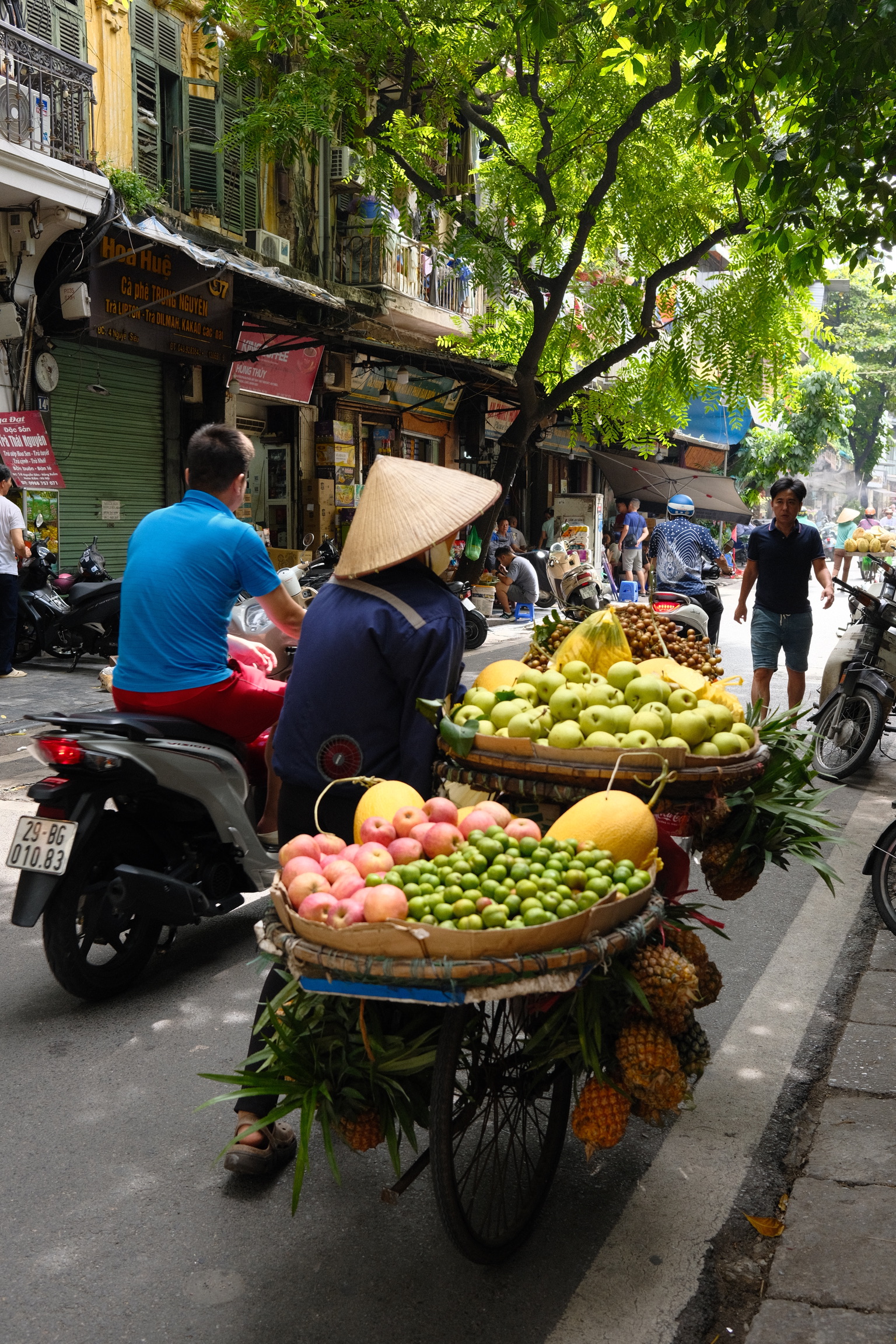 Street scene with people carrying baskets of fruit on a bicycle.
