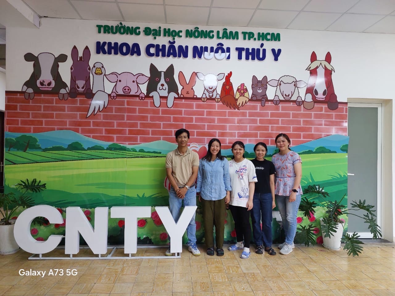 A group of people standing in front of a sign with painted animals looking over a wall.