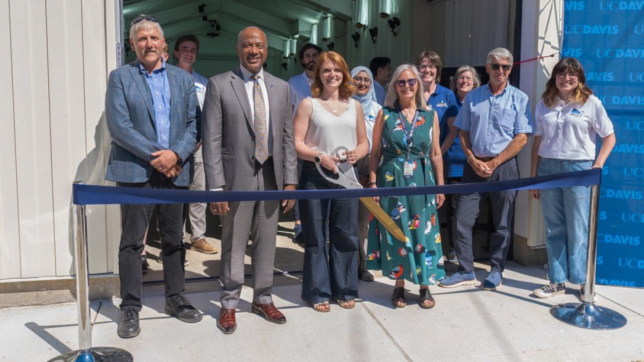 Diverse group of smiling people at blue ribbon-cutting outside building