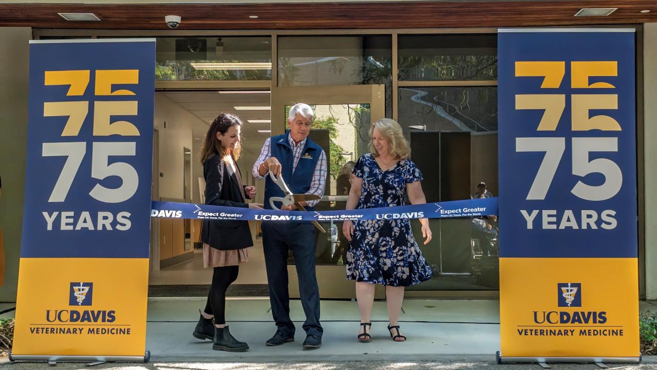three people cutting ribbon in front of building