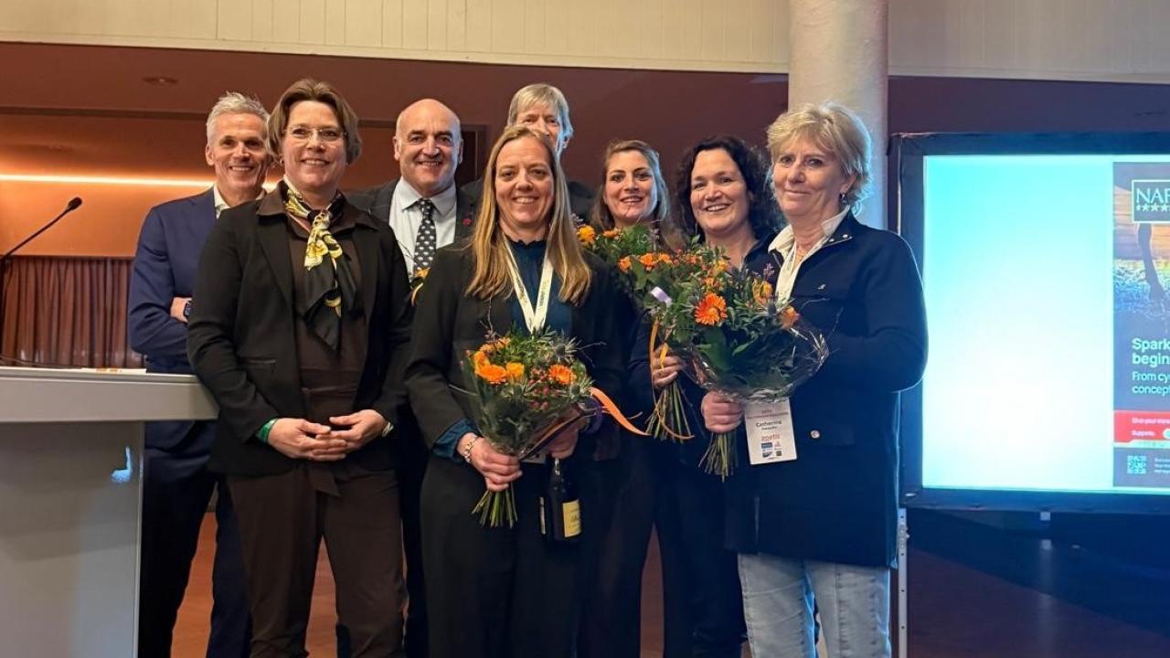 Group of individuals smiling together, holding flowers, celebrating an achievement indoors.