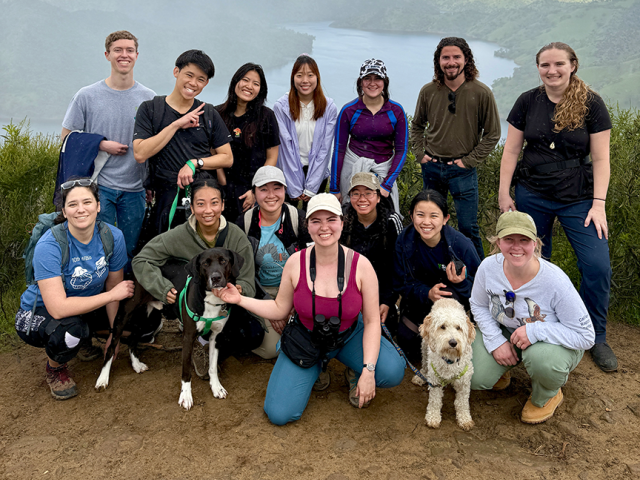 A group of students pose at the top of a hill overlooking a lake.
