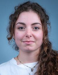 Young woman portrait, curly brown hair, septum ring, neutral expression, blue background