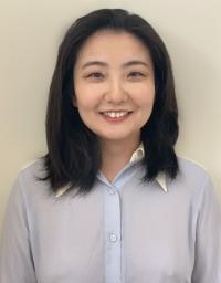 Smiling woman with shoulder-length dark hair in light blouse against neutral background