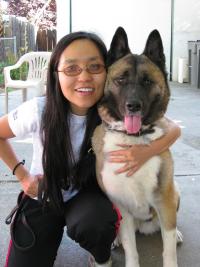 Smiling woman with glasses crouching beside large tan-and-black dog on sunlit patio
