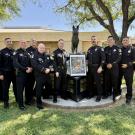 Uniformed police gathered around memorial pedestal with framed photo and bronze statue
