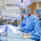 Surgical team in blue scrubs operating on covered patient in bright OR — photograph