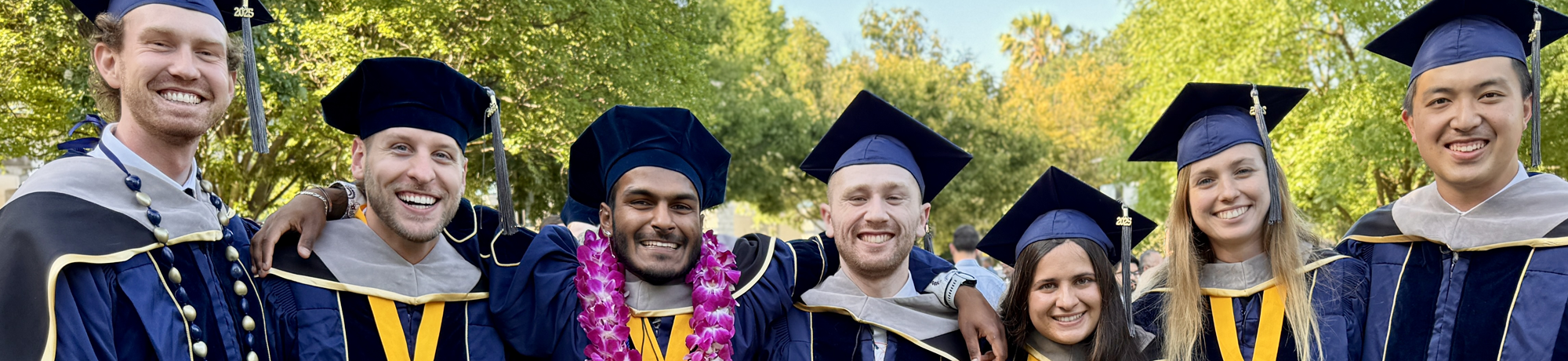 A group of graduates wearing caps and gowns posing outside.